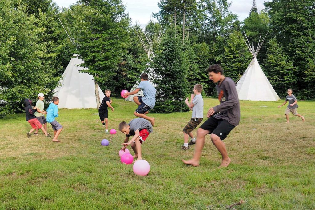 Boys playing dodgeball near tipis