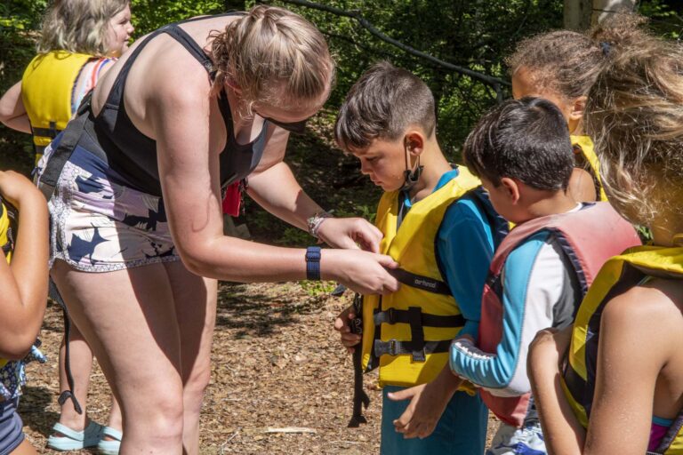 Counselor helping camper with life vest