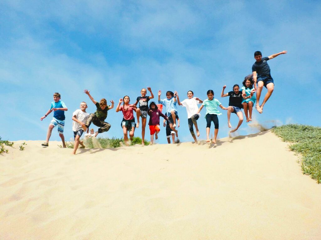 Group of campers jumping on sand dune