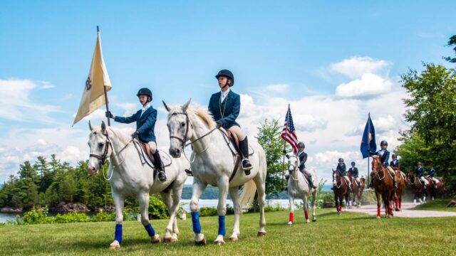 Campers riding horses holding flags