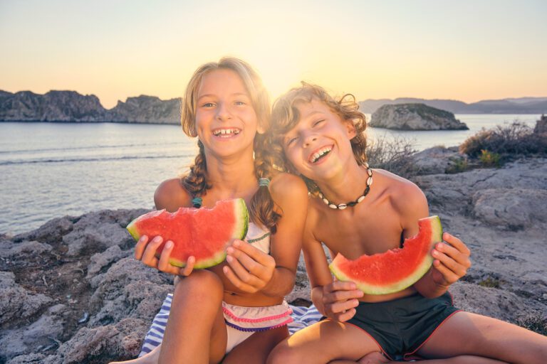 Two kids sitting eating watermelon