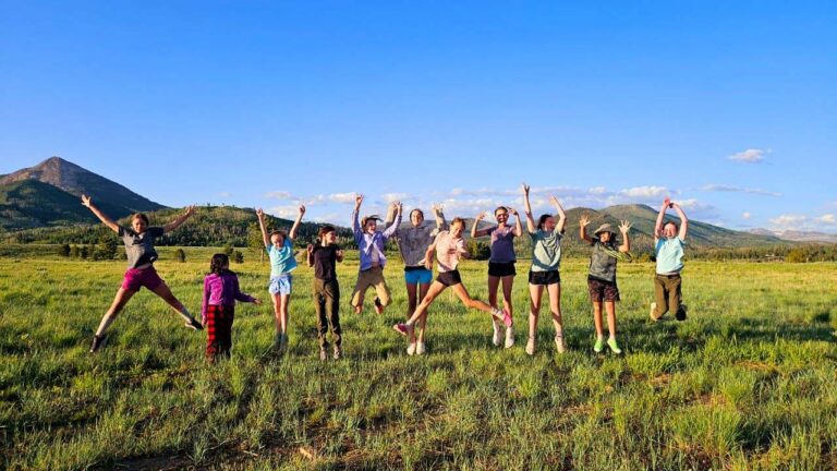 Campers jumping in air together with mountain behind them